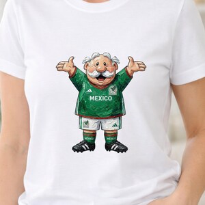 May include: A white short-sleeved t-shirt featuring a graphic of a cartoon character with a white mustache wearing a green Mexico soccer jersey, white shorts, and black cleats. The character has arms outstretched and the word MEXICO is printed on the chest.