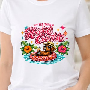 May include: A white t-shirt featuring a graphic of a brown dachshund wearing a straw hat and sunglasses, floating on a pink leopard-print inner tube in blue water. The text reads "HOTTER THAN A Hoochie Coochie" with hibiscus flowers.
