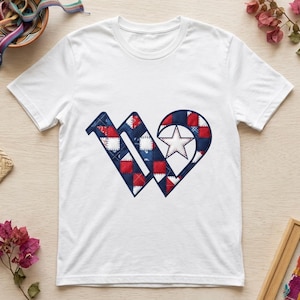 Puede incluir: Una camiseta blanca de manga corta con un gráfico grande de la letra W en el pecho. La letra está rellena con un patrón de patchwork acolchado en rojo, blanco y azul e incluye una forma de estrella blanca integrada en el lado derecho.