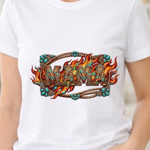 Puede incluir: Una camiseta blanca de manga corta con un estampado gráfico de la palabra MAMA en una fuente con patrones. El texto está rodeado por un borde de cuerda marrón con detalles en turquesa y llamas estilizadas en naranja, rojo y azul.