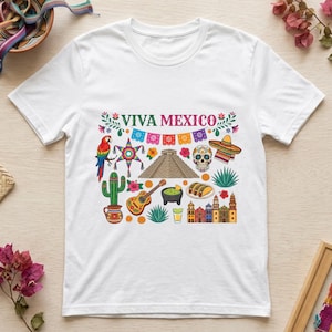 Puede incluir: Una camiseta blanca de manga corta con un estampado gráfico colorido y el texto VIVA MEXICO. El diseño incluye un loro, una piñata en forma de estrella, una pirámide, una calavera de azúcar, un sombrero, un cactus, una guitarra y tacos.