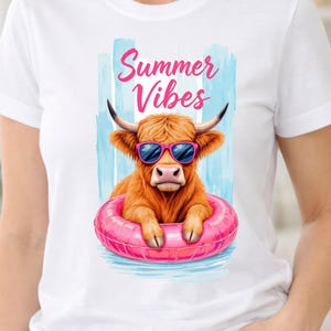 Puede incluir: Una camiseta blanca de manga corta con un gráfico de una vaca Highland marrón con gafas de sol rosas. La vaca está dentro de un flotador inflable de color rosa brillante. Sobre la vaca, el texto Summer Vibes está impreso en letra cursiva rosa.