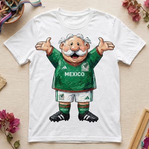 Puede incluir: Una camiseta blanca de manga corta con el gráfico de un personaje de dibujos animados con bigote blanco, vistiendo una camiseta de fútbol verde de México, pantalones cortos blancos, calcetines verdes y botas negras con los brazos abiertos.