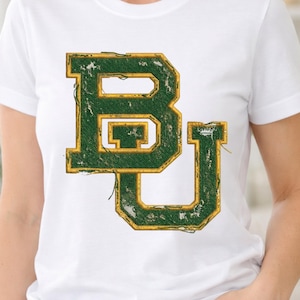 May include: White t-shirt featuring a distressed green and gold "BU" collegiate logo. The logo has a textured, vintage appearance. The shirt is made of a soft, lightweight material.