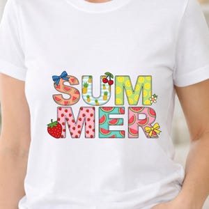 Puede incluir: Una camiseta blanca de manga corta con la palabra SUMMER en letras grandes. Cada letra tiene un patrón único: rodajas de sandía, piñas, cerezas, limones y fresas. El diseño incluye un lazo azul y un lazo amarillo decorativos.