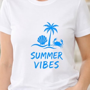 Puede incluir: Una camiseta blanca de manga corta con un estampado gráfico en azul brillante. El diseño incluye una palmera, una concha y un cangrejo sobre líneas onduladas. Debajo del gráfico, el texto "SUMMER VIBES" está impreso en una fuente azul.