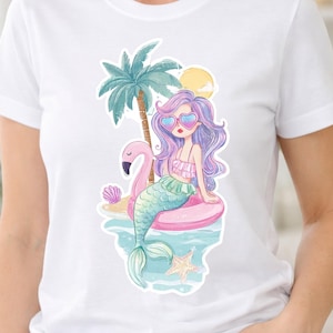 Puede incluir: Una camiseta blanca con una ilustración gráfica de una sirena de pelo largo morado con gafas de sol en forma de corazón. La sirena está sentada sobre un flotador rosa junto a un flamenco inflable, una palmera, un sol amarillo y una estrella de mar.