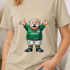 May include: A beige t-shirt featuring a cartoon illustration of an elderly character with a white mustache wearing a green and white Mexico soccer jersey, white shorts, green socks, and black cleats with the text MEXICO printed on the chest.