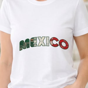 Puede incluir: Una camiseta blanca de manga corta con la palabra MEXICO impresa en el pecho. Cada letra está rellena con un patrón de patchwork distinto en tonos verde, crema y rojo, creando un diseño gráfico colorido sobre la tela blanca lisa.