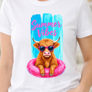 Puede incluir: Una camiseta blanca con un gráfico de una vaca Highland marrón con gafas de sol rosas. La vaca está dentro de un flotador inflable de color rosa brillante. Detrás hay tres pinceladas azules verticales y el texto Summer Vibes en color rosa.
