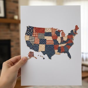 Puede incluir: Una impresión del mapa de los Estados Unidos, elaborado con tela de retazos en patrones rojos, blancos y azules. El mapa incluye Alaska y Hawái. La obra de arte se muestra sobre un fondo blanco.
