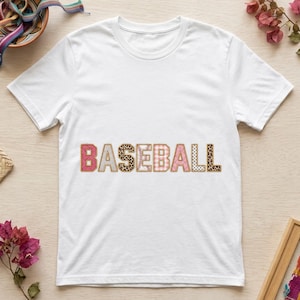 Puede incluir: Una camiseta blanca de manga corta con la palabra BASEBALL impresa en el pecho. Cada letra tiene un patrón único, incluyendo rayas rosas, gris, estampado de leopardo, costuras de béisbol, cuadros rosas, lunares rosas y estampado de leopardo.