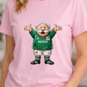 May include: A light pink short-sleeved t-shirt featuring a graphic of a cartoon character with a white mustache wearing a green and white Mexico soccer jersey, white shorts, green socks, and black cleats with the word MEXICO printed on the chest.