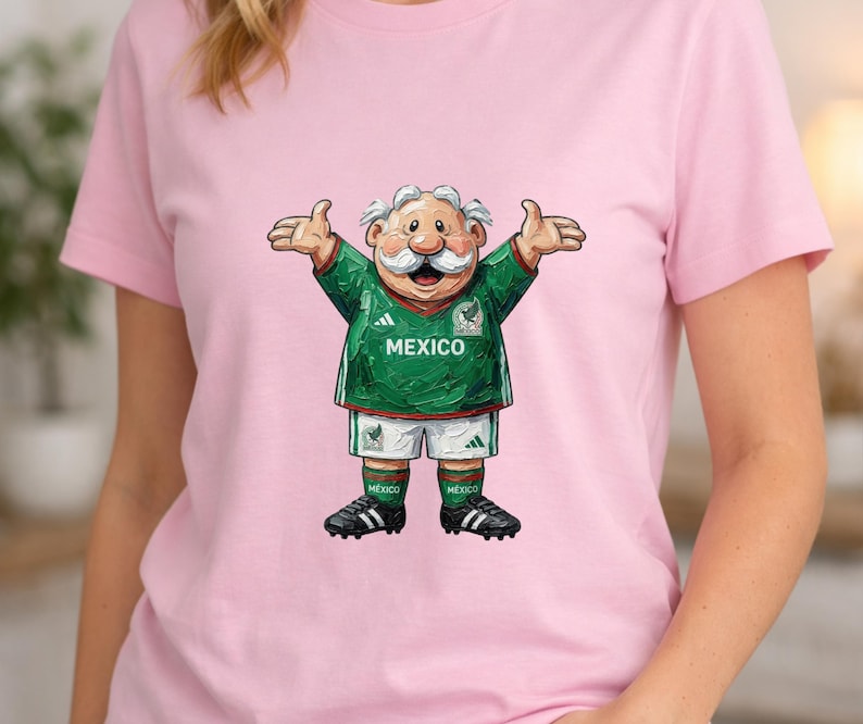 May include: A light pink short-sleeved t-shirt featuring a graphic of a cartoon character with a white mustache wearing a green and white Mexico soccer jersey, white shorts, green socks, and black cleats with the word MEXICO printed on the chest.