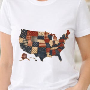 Puede incluir: Camiseta blanca con un diseño de patchwork del mapa de los Estados Unidos. El mapa está compuesto por varios patrones de tela en rojo, blanco y azul, incluyendo estrellas, rayas y cuadros. La camiseta es de estilo cuello redondo clásico.
