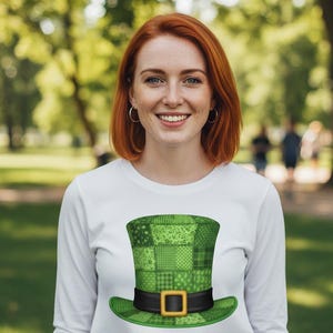 Puede incluir: Camiseta blanca de manga larga con un diseño de sombrero de duende verde en patchwork. El sombrero tiene una banda negra y una hebilla dorada. Ideal para el Día de San Patricio.