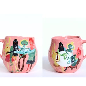 Könnte beinhalten: Rosa Keramikbecher mit einem skurrilen Design. Der Becher hat einen Henkel und ist mit farbenfrohen Illustrationen von Cartoonfiguren in verschiedenen Posen verziert. Die Figuren umfassen Charaktere mit schwarzen, grünen und roten Merkmalen. Der Becher hat eine einzigartige, strukturierte Oberfläche.