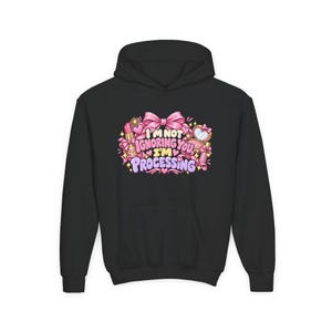 May include: A black hoodie featuring a graphic print with the text "I'M NOT IGNORING YOU, I'M PROCESSING" in pink and purple letters. The design includes illustrations of pink bows, lipsticks, a compact mirror, and small yellow stars.