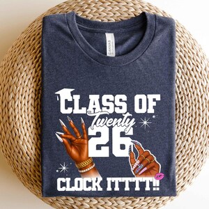 May include: Dark blue t-shirt with the text "CLASS OF Twenty 26 CLOCK ITTTT!!" in white. The design includes illustrations of hands with long, manicured nails, a graduation cap, and a pink lip.