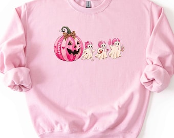 May include: A light pink crewneck sweatshirt featuring a graphic print of a large pink pumpkin with a leopard print bow, followed by three small ghosts wearing pink football helmets and holding football-themed items, all in a soft pastel palette.