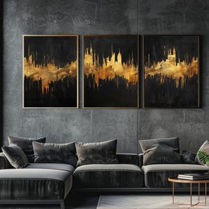Puede incluir: Tres obras de arte abstractas enmarcadas. Cada una presenta un fondo negro con pinceladas doradas, creando un diseño similar a un paisaje urbano. La obra de arte se exhibe sobre un sofá seccional gris oscuro.