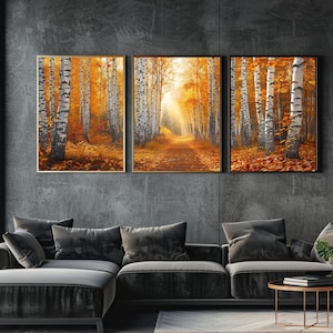 May include: Three framed landscape paintings depicting a forest scene in autumn. The artwork features birch trees with white bark and orange and yellow foliage. The paintings are displayed above a dark gray sectional sofa.