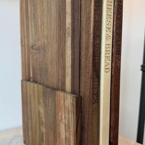 May include: A wooden cutting board set with three boards labeled "Fruits & Vegetables", "Cheese & Bread", and "Meat & Fish". The boards are made of different wood tones and are stacked together in a vertical arrangement.