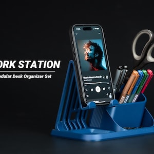 Peut inclure: Un ensemble d'organisateur de bureau modulaire bleu avec un smartphone affichant une application musicale, des stylos et des ciseaux. Le texte "WORK STATION" et "Modular Desk Organizer Set" sont affichés.