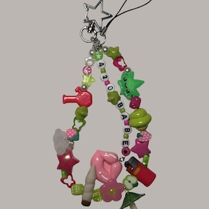 May include: A beaded phone charm with a star-shaped clasp. The charm features green, pink, and white beads, with charms shaped like stars, lips, a lighter, and a mushroom. The text "420 BABE" is spelled out with letter beads.