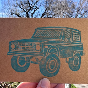 May include: A white ceramic mug with a black handle and the text "But First, Coffee" in a black, handwritten-style font. The mug is on a white surface.