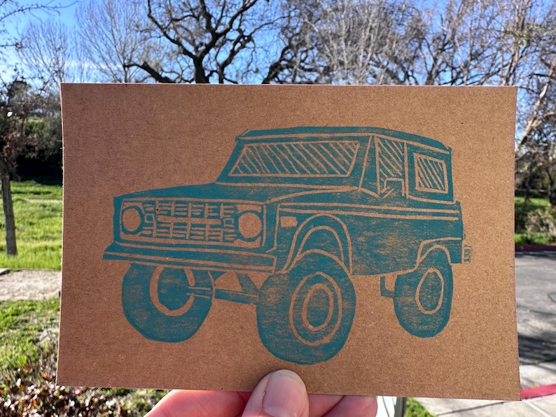 May include: A white ceramic mug with a black handle and the text "But First, Coffee" in a black, handwritten-style font. The mug is on a white surface.