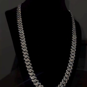 May include: A sparkling silver chain necklace with a cuban link design. The necklace is displayed on a black velvet bust. The text "MDJewellers" is visible at the bottom of the image.