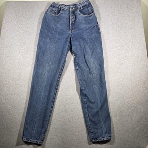 May include: High-waisted blue denim jeans featuring a button-fly closure, two front pockets, and a tapered leg silhouette. The medium-wash fabric has a classic texture with visible stitching along the seams and a structured waistband.