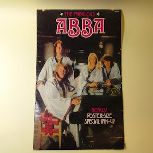 Pode incluir: Uma capa de revista vintage intitulada The Fabulous ABBA com uma fotografia dos quatro membros da banda em vestes brancas. Um membro está sentado a um piano preto enquanto os outros estão atrás. Texto: Bonus! Poster-Size Special Pin-Up.