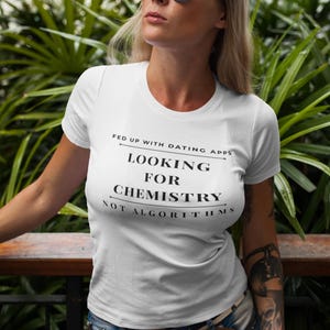 May include: White t-shirt with the text "FED UP WITH DATING APPS LOOKING FOR CHEMISTRY NOT ALGORITHMS". The person is wearing blue mirrored sunglasses and blue jeans.