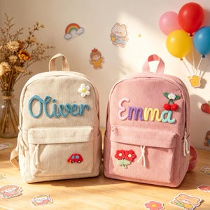 May include: Two corduroy backpacks, one beige and one pink, are displayed. The beige backpack has the name "Oliver" in blue, a white flower, and a red car patch. The pink backpack has the name "Emma" in colorful letters, a cherry patch, and a flower patch.