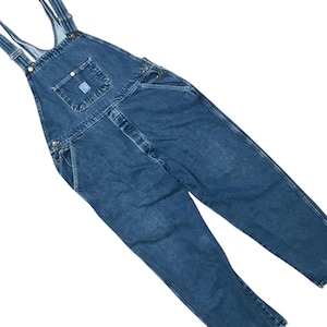 May include: Dark blue denim overalls featuring a front bib pocket with a small rectangular patch, adjustable shoulder straps with metal buckles, side hip pockets, and metal buttons along the sides. The fabric has a slightly faded wash finish.