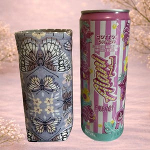 Op de afbeelding: Een stoffen drankhoes met een vlinder- en bloemenpatroon naast een Cotton Candy-gearomatiseerde energiedrankblik. Het blik is roze en wit gestreept met het woord "Energy" in een neonstijl.