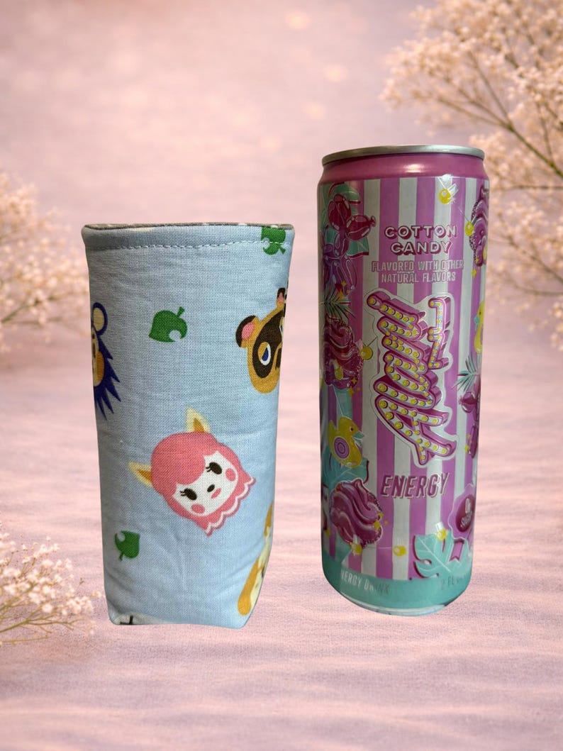 Op de afbeelding: Een lichtblauwe drankhoes met stripfiguren en bladeren. Daarnaast staat een roze en wit gestreepte energiedrankblik met de woorden "Cotton Candy" en "Energy".