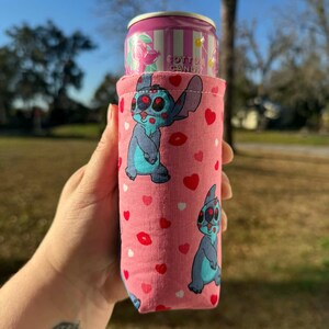 May include: Pink can cooler featuring a blue cartoon character with red eyes and a pink background with red hearts and lips. A pink can with "Cotton Candy" text is inside the cooler.