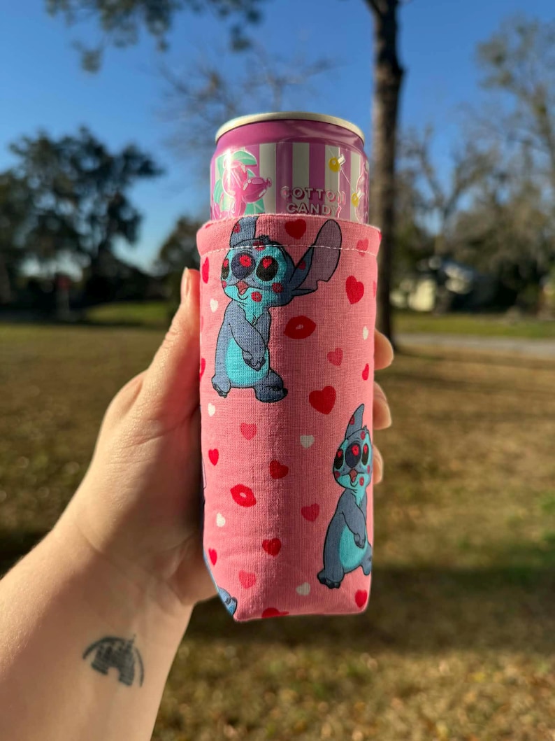 May include: Pink can cooler featuring a blue cartoon character with red eyes and a pink background with red hearts and lips. A pink can with "Cotton Candy" text is inside the cooler.