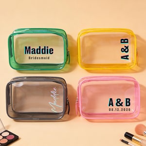 May include: Four clear, rectangular cosmetic bags with coloured trim in green, yellow, grey, and pink. Each bag has a zip closure and personalised text: "Maddie Bridesmaid", "A & B", "Maddie", and "A & B 08.12.2026".