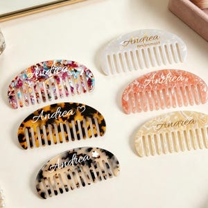 Può includere: Sei pettini per capelli semicircolari con vari motivi, tra cui coriandoli multicolori, tartarugato e bianco tinta unita. Ogni pettine riporta il nome Andrea in corsivo, alcuni decorati con simboli aggiuntivi come un cuore o un fiore.