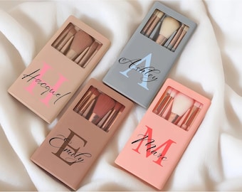 May include: Four rectangular makeup brush cases in beige, gray, brown, and peach, each featuring a clear window displaying brushes inside. The cases are personalized with large block letters and cursive names: Hacquel, Ashley, Emily, and Marc.