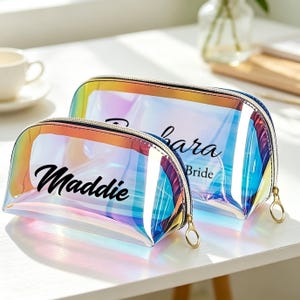Peut inclure: Deux trousses de maquillage irisées avec des fermetures éclair dorées. Le plus petit sac porte le nom "Maddie" imprimé en écriture noire. Le plus grand sac porte le nom "Kara" et le mot "Bride" imprimés en écriture noire.