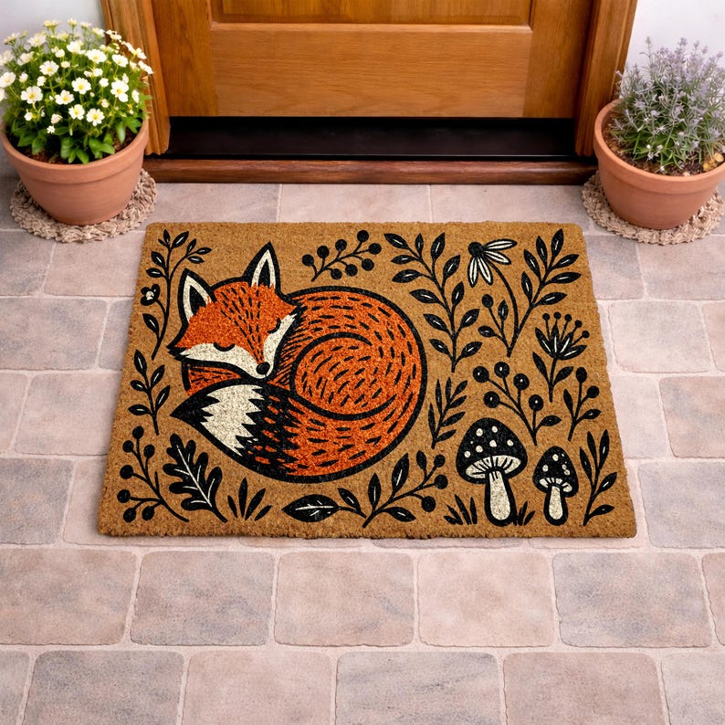 A decorative door mat with a fox curled up and surrounded by leaves and mushrooms, placed on a tiled floor near a wooden door.