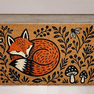 A decorative door mat with a fox curled up and surrounded by various plants and mushrooms.