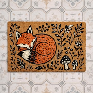 A decorative door mat with a fox curled up and surrounded by various plants and mushrooms.