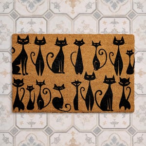 May include: A rectangular doormat made of natural coir fiber, featuring a repeating pattern of stylized black cat silhouettes. The cats are in various poses, adding a whimsical touch to the entryway decor. The mat is designed for outdoor use.