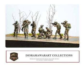 Op de afbeelding: Een diorama met handgeschilderde militaire modellen van hars in camouflage-uniformen. De scène toont soldaten in actie, waaronder het dragen van een gewonde kameraad. De modellen staan tegen een achtergrond van schaarse vegetatie.